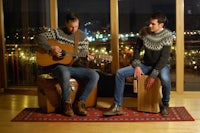 two men playing guitars in front of a window